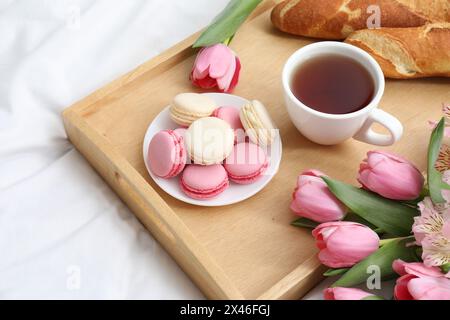 Leckeres Frühstück im Bett. Köstliche Macarons, Tee, Baguette und Blumen auf dem Tablett Stockfoto