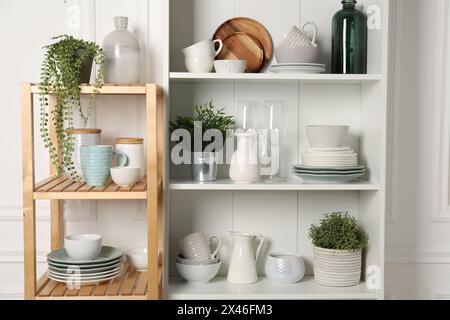 Verschiedene saubere Geschirr und Zimmerpflanzen auf den Regalen im Schrank drinnen Stockfoto