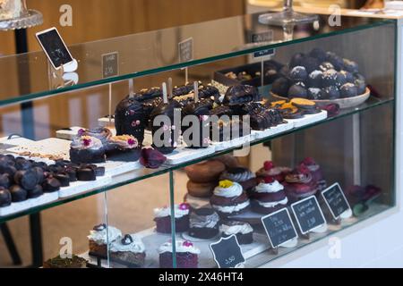 Verschiedene leckere vegane Desserts auf Glasregalen der Vitrine in der hellen Bäckerei platziert Stockfoto