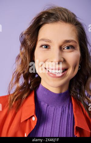 Eine stilvolle junge Frau hebt sich in einer leuchtend orangefarbenen Jacke vor einem violetten Hintergrund ab. Stockfoto