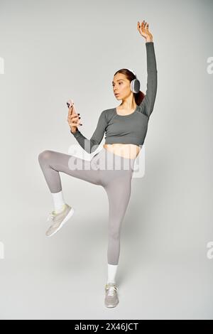 Eine sportliche junge Frau in grauer Hose und grauem Oberteil steht selbstbewusst vor grauem Hintergrund. Stockfoto