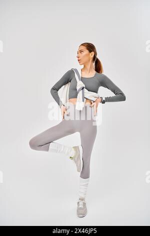 Eine sportliche junge Frau in grau-weißer Aktivkleidung posiert auf grauem Hintergrund. Stockfoto