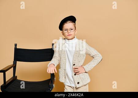 Ein süßer Junge, der als Filmregisseur gekleidet ist und neben einem Stuhl steht. Stockfoto