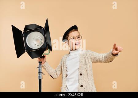 Ein süßer Junge, der als Filmregisseur verkleidet ist, eine Kamera und ein Licht hält. Stockfoto