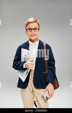Ein kleiner Junge in Brille und blauem Blazer strahlt Eleganz vor grauem Hintergrund aus. Stockfoto
