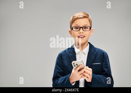 Eleganter vorpubertärer Junge in Brille mit Handy auf grauem Hintergrund. Stockfoto