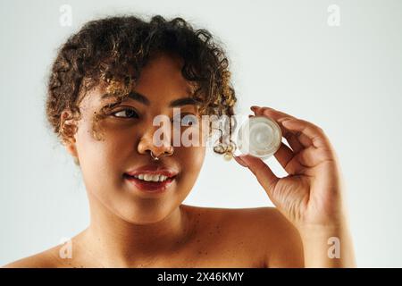 Eine afroamerikanische Frau hält eine Creme-Flasche in ihrer rechten Hand vor einem lebendigen Hintergrund elegant. Stockfoto