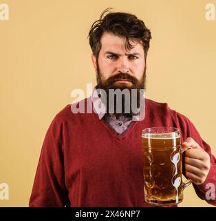 Bierzeit. Ernsthafter Mann mit Bart und Schnurrbart, der Bier in einer Kneipe oder Bar trinkt. Alkohol. Stilvoller bärtiger Mann mit einer Tasse Bier. Gutaussehendes männliches Verkostungsgewerbe Stockfoto