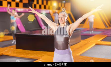 Energiegeladene europäische Frau in aktiver Kleidung posiert auf Trampolinen während des aktiven Wochenendes in der Sportzentrale Stockfoto
