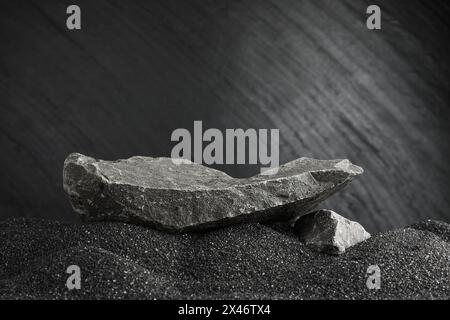 Aufmachung des Produkts. Steinpodium auf schwarzem Sand vor dunklem, strukturiertem Hintergrund. Leerzeichen für Text Stockfoto