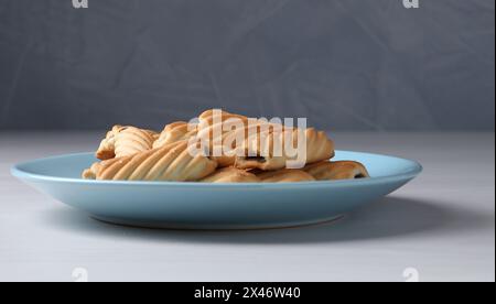 Frau mit einem Sieb, das Puderzucker auf Kekse streut, an weißem Holztisch, Nahaufnahme Stockfoto
