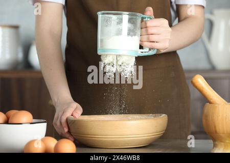 Frau siebt Mehl in eine Schüssel am Tisch in der Küche, Nahaufnahme Stockfoto