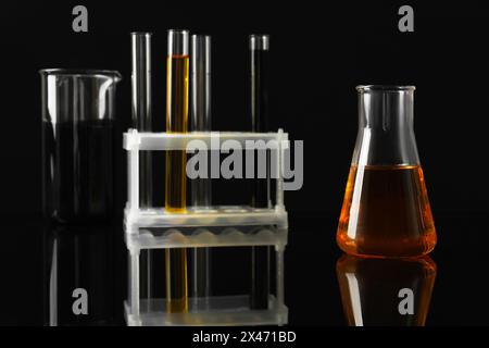 Laborglas mit verschiedenen Ölsorten auf schwarzem Hintergrund, Nahaufnahme Stockfoto