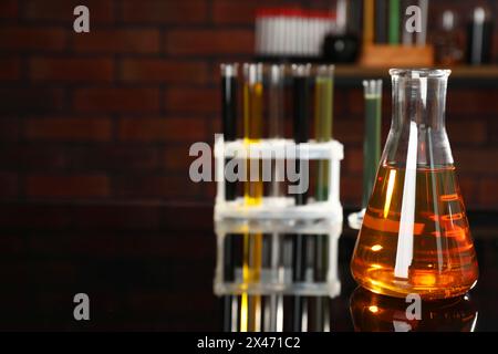 Laborglas mit verschiedenen Ölsorten auf schwarzem Spiegeltisch im Innenbereich, Nahaufnahme. Leerzeichen für Text Stockfoto
