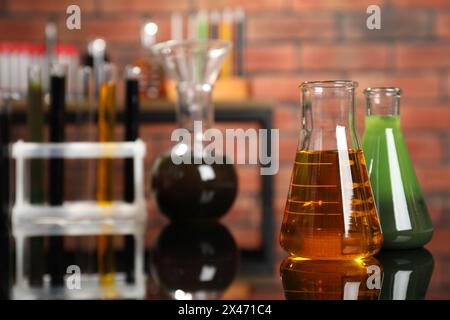 Laborglas mit verschiedenen Ölsorten auf Spiegeltisch im Innenbereich, Nahaufnahme Stockfoto