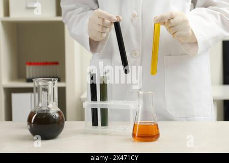 Laborarbeiter, der Reagenzgläser mit verschiedenen Rohölsorten am hellen Marmortisch hält, Nahaufnahme Stockfoto