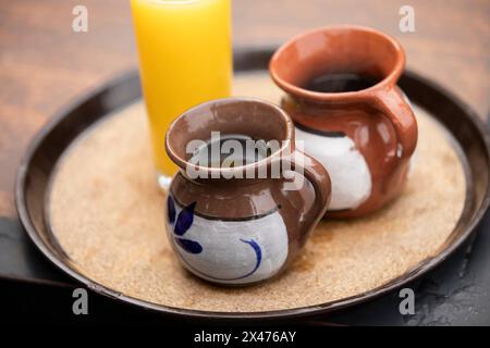 Zwei Tassen spezieller mexikanischer Kaffee, Café de olla, serviert in Tonbechern zusammen mit einem Glas Orangensaft auf einem Tablett in Bernal, Querétaro, Mexiko. Stockfoto