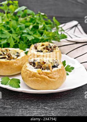 Brötchen gefüllt mit Pilzen, Zwiebeln und Käse in Teller, Petersilie und Serviette auf dunklem Holzbrett Stockfoto