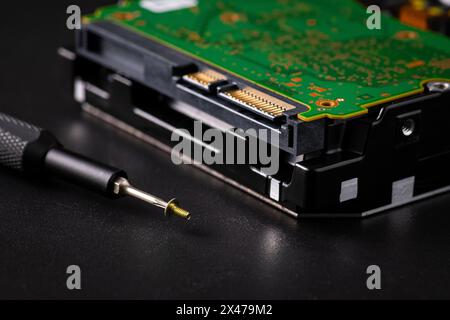 Festplatte und Leiterplatte mit SATA-Netzanschluss. Magnetschrauber, torx-Bit und kleine Maschinenschraube auf dunklem Hintergrund. Stockfoto