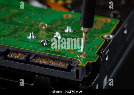 Festplatte und Leiterplatte mit SATA-Netzanschluss. Magnetschrauber, torx-Bit und kleine Maschinenschraube auf dunklem Hintergrund. Stockfoto