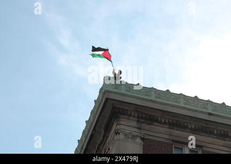 Ein pro-palästinensischer Demonstrant schwingt die palästinensische Flagge vom Dach der Hamilton Hall der Columbia University. Pro-palästinensische Demonstranten versammelten sich vor einem der Eingänge der Columbia University in Manhattan, New York City, und verurteilten die Militäroperationen der israelischen Streitkräfte in Gaza. Seit fast zwei Wochen haben Studenten und pro-palästinensische Aktivisten der Columbia University einen Sit-in-Protest auf dem Campus abgehalten und ein "Gaza Solidarity Encamp" gebildet. Über Nacht besetzten Studenten und Demonstranten auf dem Campus ein Universitätsgebäude namens Hamilton Hall und blockierten die Eingänge. Universitätsadministratoren Stockfoto