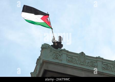 Ein pro-palästinensischer Demonstrant schwingt die palästinensische Flagge vom Dach der Hamilton Hall der Columbia University. Pro-palästinensische Demonstranten versammelten sich vor einem der Eingänge der Columbia University in Manhattan, New York City, und verurteilten die Militäroperationen der israelischen Streitkräfte in Gaza. Seit fast zwei Wochen haben Studenten und pro-palästinensische Aktivisten der Columbia University einen Sit-in-Protest auf dem Campus abgehalten und ein "Gaza Solidarity Encamp" gebildet. Über Nacht besetzten Studenten und Demonstranten auf dem Campus ein Universitätsgebäude namens Hamilton Hall und blockierten die Eingänge. Universitätsadministratoren Stockfoto