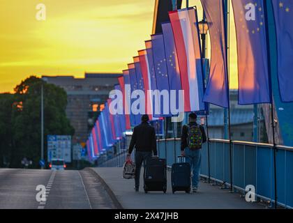 1. Mai 2024, Brandenburg, Frankfurt (oder): Zwei Reisende überqueren bei Sonnenaufgang die Stadtbrücke über die oder-Grenze zwischen Frankfurt (oder) und Slubice in Polen. Die Außenminister der beiden Nachbarländer wollen sich mittags zum 20. Jahrestag des EU-Beitritts Polens treffen. Beide wollen das Collegium Polonicum in Slubice auf polnischer Seite besuchen, sowie ein europäisches Festival, und dann gemeinsam über die Stadtbrücke über die deutsch-polnische Grenze oder nach Frankfurt (oder) laufen. Foto: Patrick Pleul/dpa Stockfoto