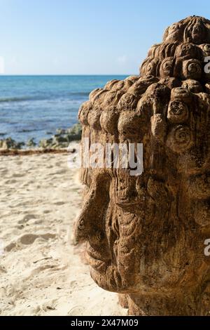 Nahaufnahme des Gesichts der Buddha-Statue an einem tropischen Strand mit Blick auf das Meer, Palmen und Hängematten im Hintergrund Stockfoto