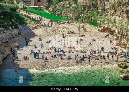 Menschen genießen den Strand in Polignano a Mare, der beliebten italienischen Strandstadt in Apulien. Sonniges Wetter im Frühjahr, Touristen und Einheimische sonnen sich Stockfoto