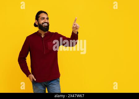 Lächelnder Mann im roten Hemd, der nach oben vor gelbem Hintergrund zeigt Stockfoto