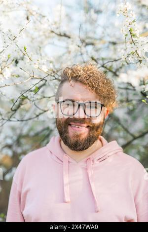 Mann mit Bart und Schnurrbart auf lächelndem Gesicht in der Nähe von Sakura-Blumen oder blühendem Frühlingsbaum. Weiches und sanftes Konzept. Bärtiger Mann mit stilvollem Haarschnitt Stockfoto