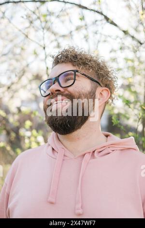 Mann mit Bart und Schnurrbart auf lächelndem Gesicht in der Nähe von Sakura-Blumen oder blühendem Frühlingsbaum. Weiches und sanftes Konzept. Bärtiger Mann mit stilvollem Haarschnitt Stockfoto