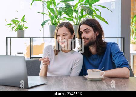 Glückliches überraschtes junges Paar, das zusammen in der Cafeteria auf den Laptop blickt Stockfoto