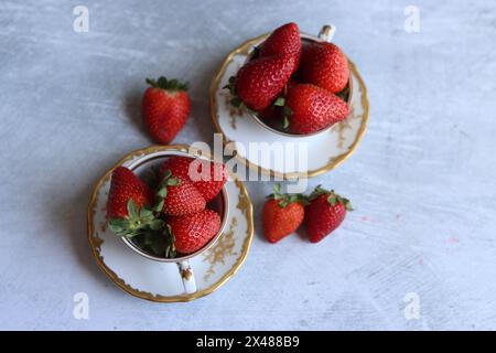 Erdbeeren in weißer Porzellanschale im Retro-Stil vor hellgrauem, strukturiertem Hintergrund mit Platz für Text. Sommersaison Bio-Obst. Frisches Essen. Stockfoto