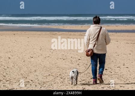 Die Rückansicht einer Frau, die mit ihrem Hund am Crantock Beach in Newquay in Cornwall in Großbritannien unterwegs ist. Stockfoto