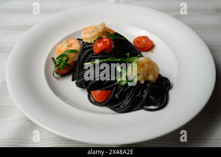 Spaghetti al Nero di Seppia con Gamberi, italienische Pasta mit Tintenfischtinte, Garnelen, Tomaten und Rucola Stockfoto