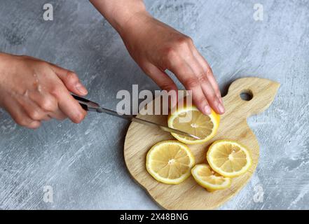 Weibliche Hände schneiden Zitronen auf einem Holzbrett auf einem grauen Hintergrund mit Platz für Text Stockfoto