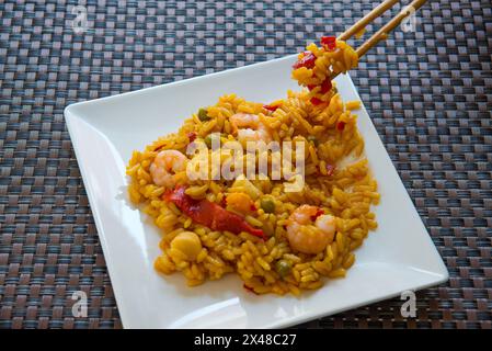 Paella valenciana gegessen mit chinesischen Essstäbchen. Stockfoto