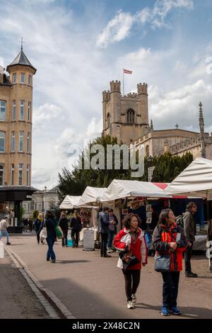 Shopper und Touristen auf einem Freiluftmarkt im Stadtzentrum von Cambridge mit dem Turm der Great Saint Marys Kirche im Hintergrund. England, Großbritannien Stockfoto