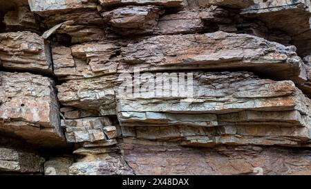 Eine felsige Klippe mit einer braunen und roten Farbe. Die Felsen stapeln sich und der Boden ist mit Schmutz bedeckt Stockfoto
