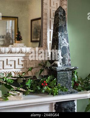 Marmorobelisk mit stechpalme und Efeu auf dem kaminsims in Dorset zu Weihnachten, England, Großbritannien Stockfoto