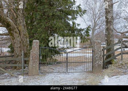 Geschlossene alte schmiedeeiserne Tore, die auf Steintorpfosten zum Friedhof im Winter in Degerby, Finnland montiert sind. Stockfoto