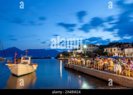 Während der schönen blauen Stunde genießen die Menschen ein Abendessen in einer lokalen Fischtaverne im malerischen Fischhafen Vathy auf der Halbinsel Methana, Griechenland. Stockfoto