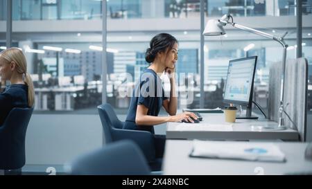 In Big Corporate Office: Beautiful Asian Business Manager, der Computer verwendet, Geschäftsleute und Experten, die um sie herum arbeiten, Statistiken, Handelsdaten und Marketingpläne analysieren. Stockfoto