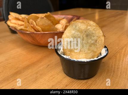 Eine Schüssel mit frisch zubereiteten Kartoffelchips und eine kleine schwarze Schüssel mit einem Dip Stockfoto