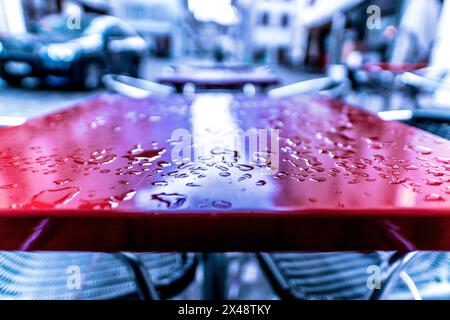 Nahaufnahme eines nassen roten Tisches eines Restaurants oder Bistros auf der Straße, nach etwas Regen. Nur ein kleiner Streifen von Wassertropfen und Pfützen konzentriert. Stockfoto