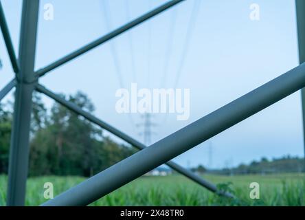 Nahaufnahme der Versteifungsstange aus Hochspannungspylon mit geringer Schärfentiefe. Unscharfer Hintergrund zeigt mehr Pylonen und das Hochspannungskabel in der Luft, ov Stockfoto