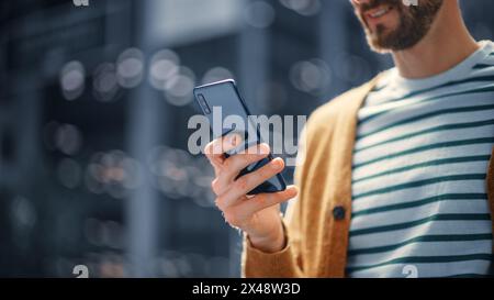 Kaukasier benutzt Smartphone in der Großstadt. Kreativer Profi mit Mobile Phone App für E-Commerce-Investitionen, Online-Shopping, soziale Medien und Surfen im Internet. Porträt Aufgenommen. Stockfoto