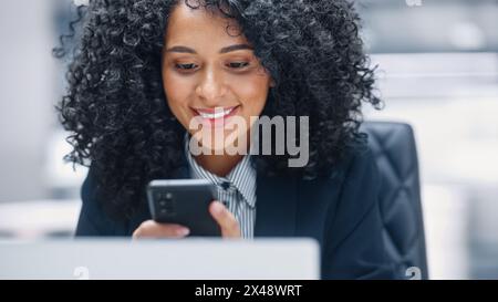 Moderner Abschluss: Schwarze Geschäftsfrau sitzt am Schreibtisch mit Smartphone. Afrikanisch-amerikanischer digitaler Unternehmer mit Mobiltelefon, Internet-E-Commerce Online-Shopping. Aufnahme mit Bewegungsunschärfe Hintergrund Stockfoto