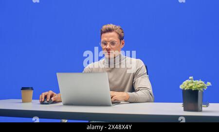 Moderner Büro-Green-Screen-Hintergrund: Junger Geschäftsmann sitzt an seinem Schreibtisch und arbeitet an einem Laptop-Computer. Mann, der mit Big Data e-Commerce-Analyse arbeitet. Stockfoto